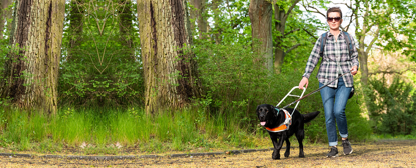 Blind woman wearing sunglasses walking through nature with sight dog