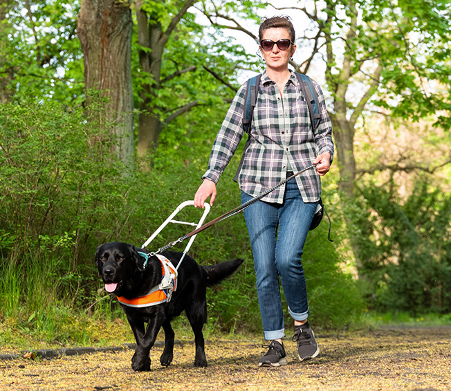 Blind woman wearing sunglasses walking through nature with sight dog