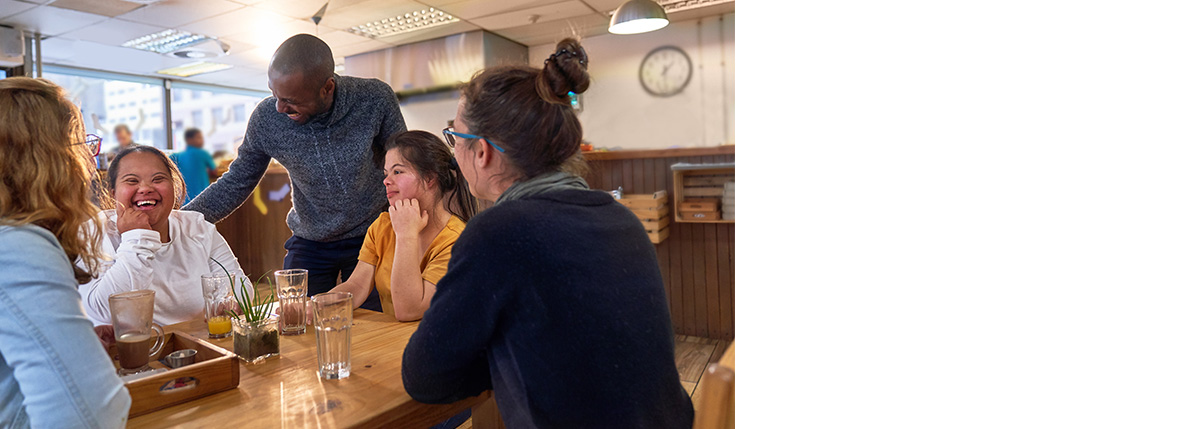 Group of friends at a cafe table talking to friendly cafe manager