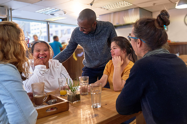 Group of friends at a cafe table talking to friendly cafe manager