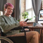 Ambiguously gendered person smiling and holding phone in wheelchair