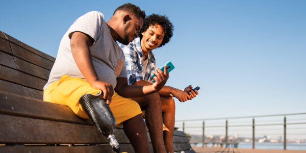 Two friends looking at phone outside on a bench, one has prosthetic leg